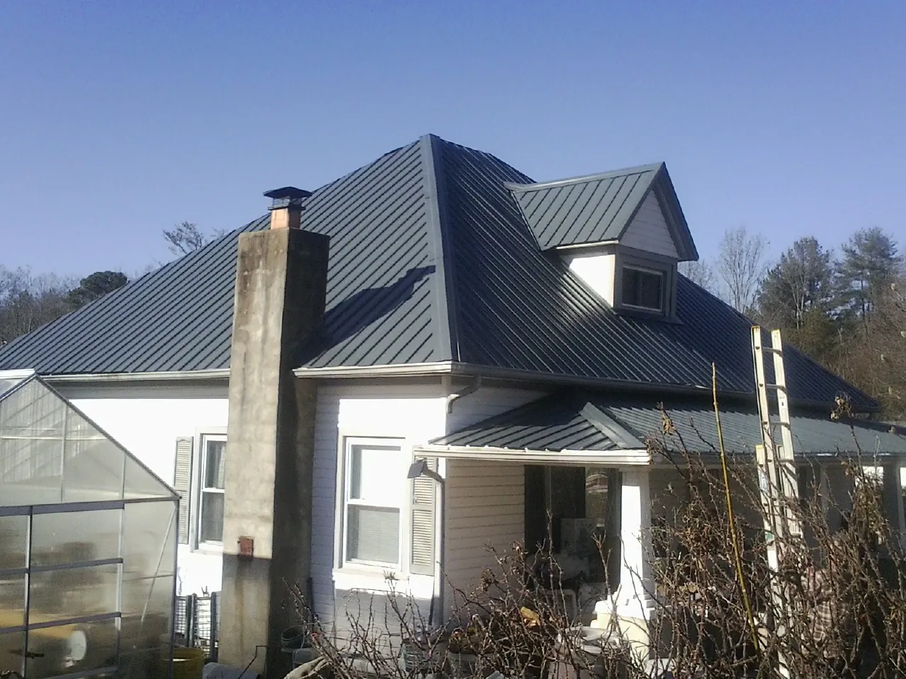Dark blue standing seam metal roof on a white farmhouse with dormer — Slate & Tile Roof Repair by Roofing Brothers in Farwell