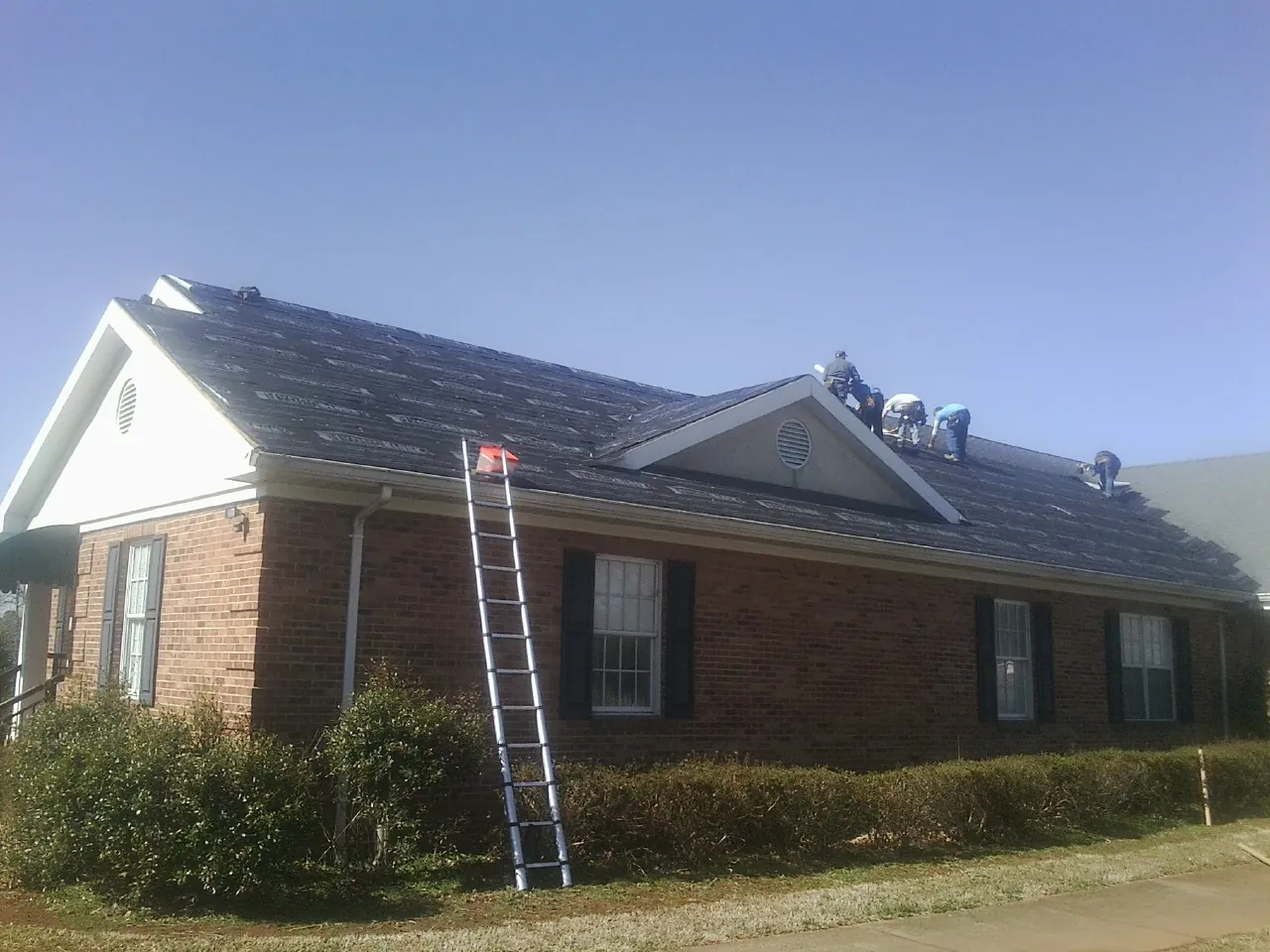 Crew tearing shingles off a brick ranch roof with a ladder set — Emergency Roof Repair work by our crew in Farwell