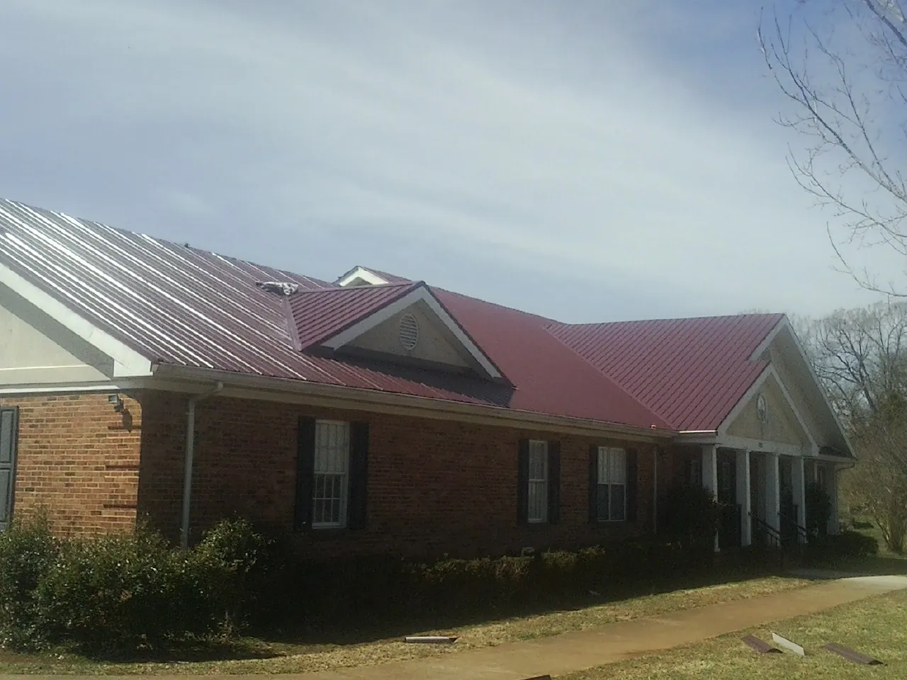 Red metal roof with gabled entries on a long brick building, from a Hail Damage Roof Repair job in Farwell