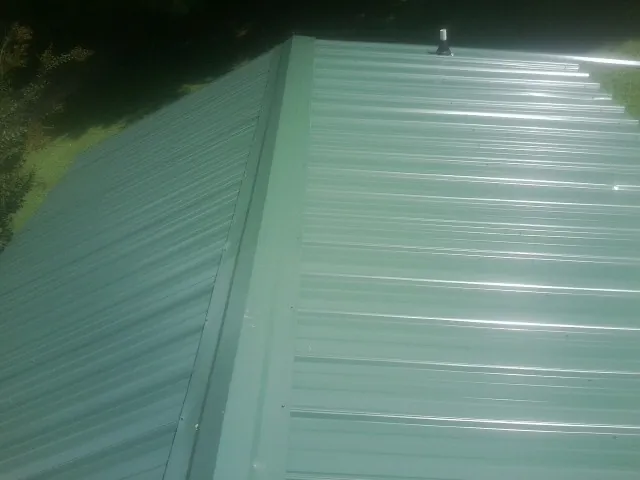 New green metal panels meeting at the ridge of a roof — Flat Roof Repair work by our crew in Farwell